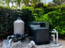 Heat pump pool heater hidden in a fenced side yard between a stucco wall and wooden fence