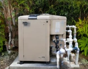 Heat pump pool heater hidden in a fenced side yard between a stucco wall and wooden fence