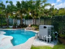 Heat pump pool heater hidden in a fenced side yard between a stucco wall and wooden fence