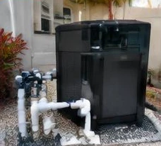 Heat pump pool heater hidden in a fenced side yard between a stucco wall and wooden fence