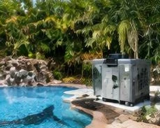 Heat pump pool heater hidden in a fenced side yard between a stucco wall and wooden fence