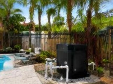 Heat pump pool heater hidden in a fenced side yard between a stucco wall and wooden fence