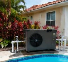 Heat pump pool heater hidden in a fenced side yard between a stucco wall and wooden fence
