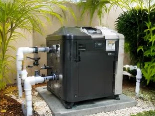 Heat pump pool heater hidden in a fenced side yard between a stucco wall and wooden fence