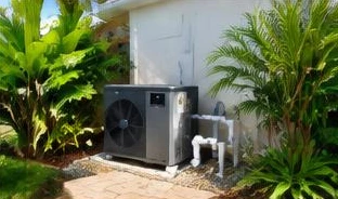 Heat pump pool heater hidden in a fenced side yard between a stucco wall and wooden fence